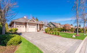 A well-kept suburban home with a paved driveway, stone pillar garage accents, and a wide lawn under a clear blue sky, illustrating a VA loan purchase.